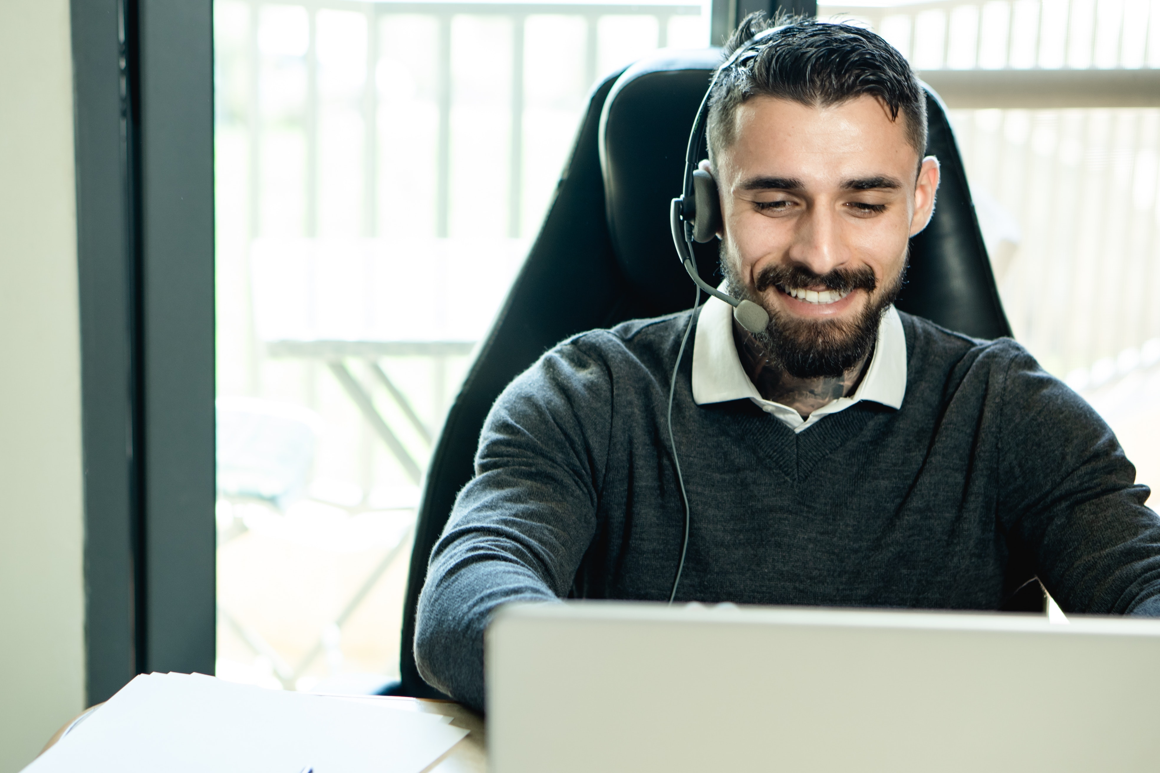 Un homme est assis devant un écran d’ordinateur. Il porte un casque d’écoute et sourit.