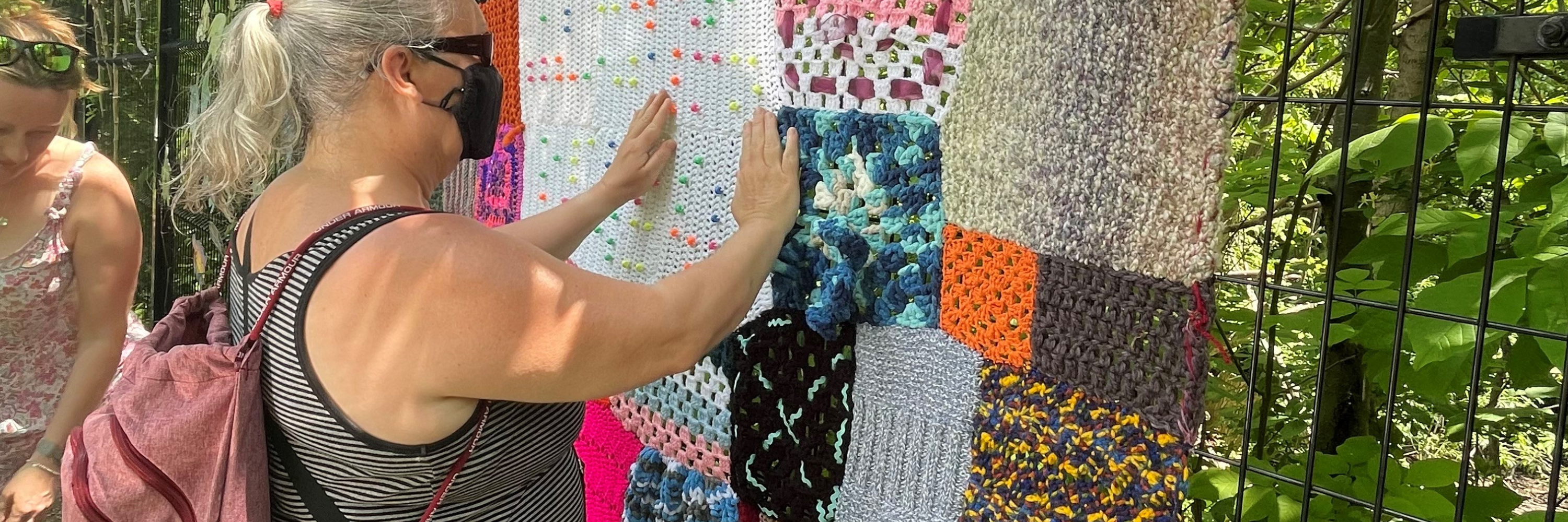 Un client de DBCS ressent la texture d'une exposition colorée de yarnbombing dans un parc local.