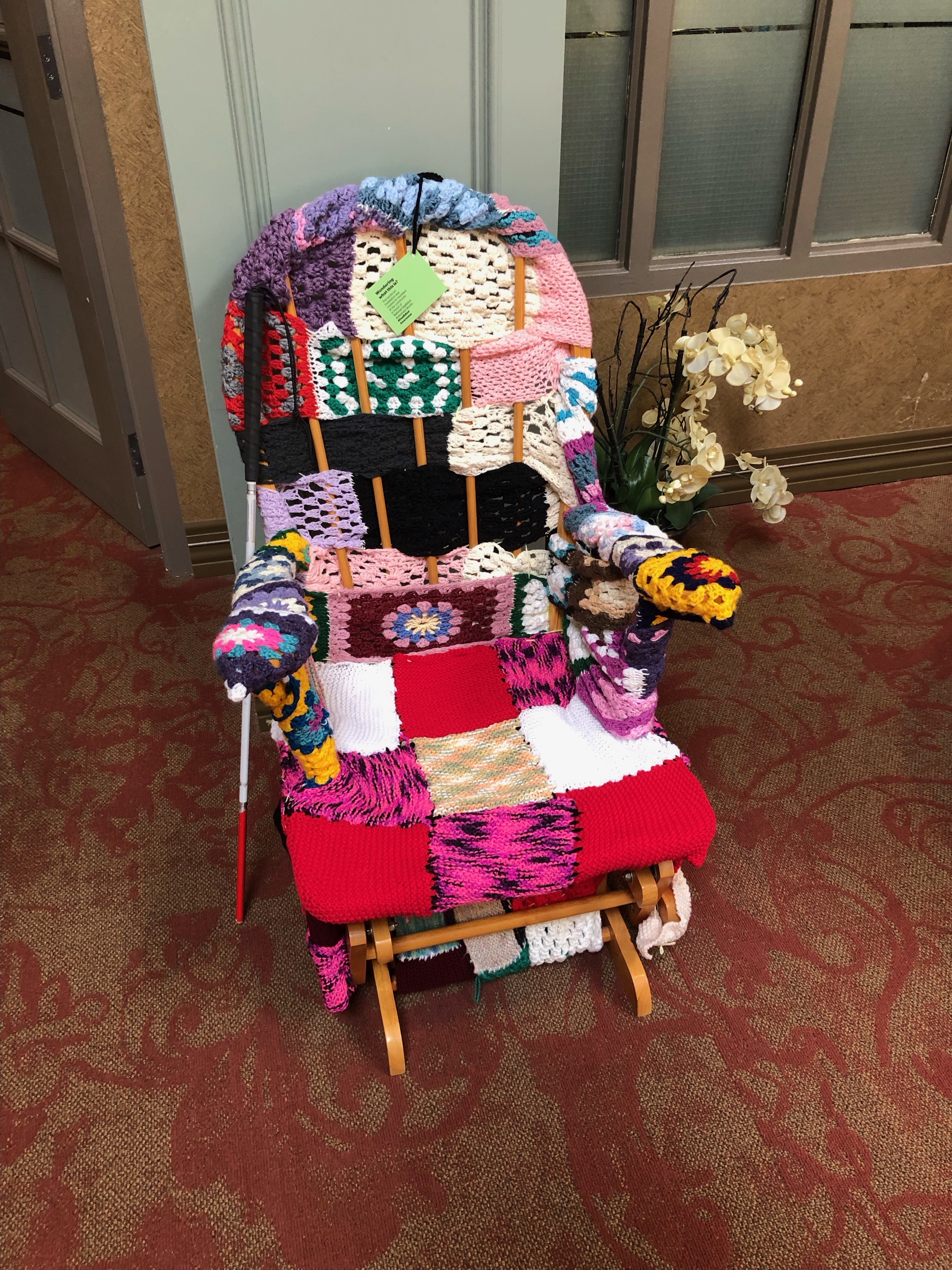 a rocking chair that has been totally covered in yarn. There is a white cane beside the chair. 