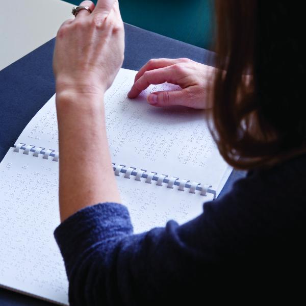 A person uses one hand to read braille, and the other to demonstrate sign language.