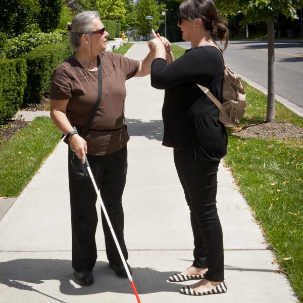 An intervenor and client stand outside and use tactile ASL to communicate.