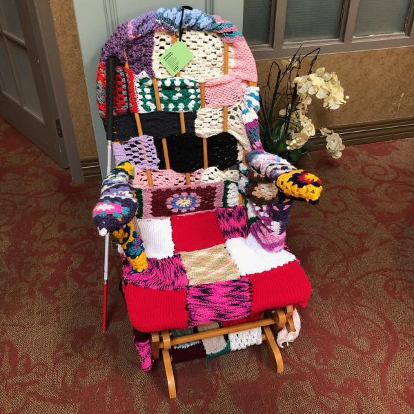 a rocking chair that has been totally covered in yarn. There is a white cane beside the chair. 